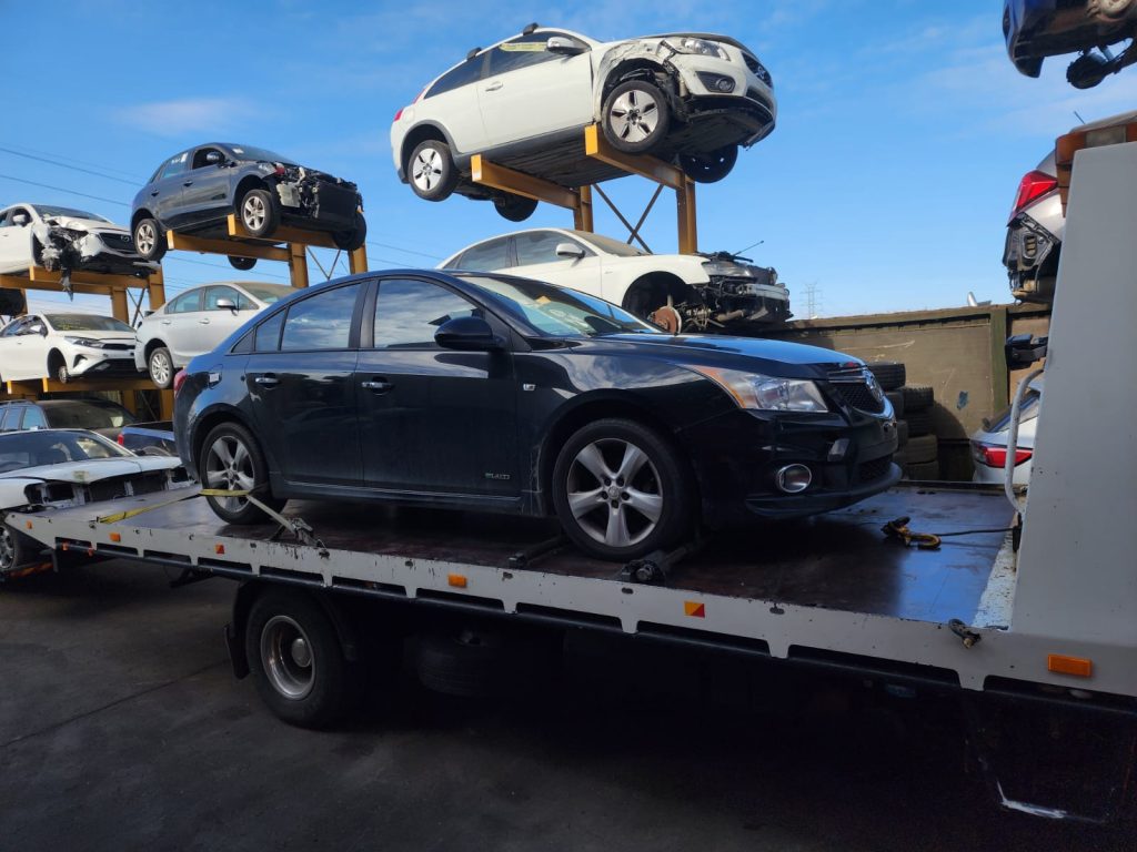 Melbourne Suburbs and Areas We Service 1 Black sedan secured on a flatbed tow truck at a vehicle recycling yard