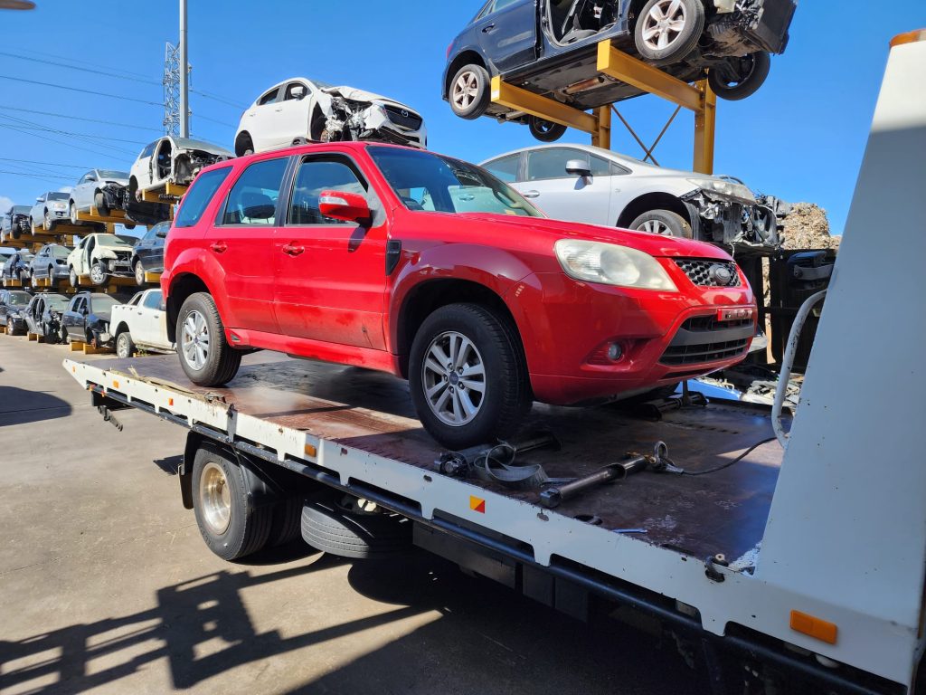 Cash for Scrap Cars Aintree VIC 1 Red SUV secured to a flatbed truck at an automotive recycling yard