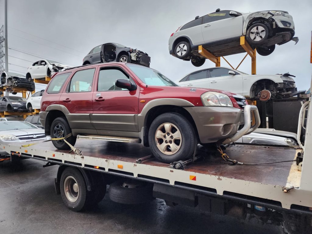 Cash for Scrap Cars Malvern VIC 1 Red and silver SUV strapped onto a flatbed truck at a vehicle yard